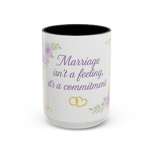 May include: White ceramic mug with a black interior, featuring the text "Marriage isn't a feeling, it's a commitment" in purple script. The design includes lavender floral accents and gold wedding ring graphics.