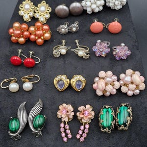 Könnte beinhalten: Eine Sammlung von Vintage-Ohrringen in verschiedenen Stilen und Farben. Enthält goldfarbene, Perlen- und Edelsteinohrringe. Einige haben florale Designs, andere eine minimalistischere Ästhetik. Die Ohrringe werden auf einer schwarzen Oberfläche präsentiert.