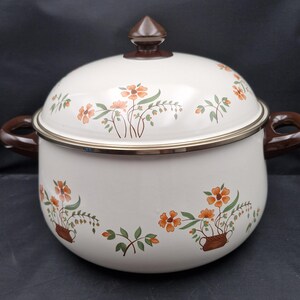 Puede incluir: Olla de esmalte color crema con tapa, asas marrones y pomo marrón. Decorada con motivos florales naranjas y verdes. Un artículo de cocina vintage.