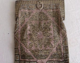 May include: An antique beaded handbag with a chain handle. The bag features a geometric design in shades of pink and gold, with a fringe at the bottom. The clasp is a metal ring. This vintage accessory is a stylish piece.