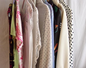 May include: A clothing rack displaying a variety of garments. The items include a floral print top, a white lace top, a polka dot shirt, and a cream-colored blouse. The clothes are hanging on plastic hangers.