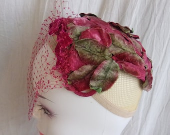 Peut inclure: Un chapeau vintage avec un motif floral. Le chapeau présente une couleur fuchsia vibrante avec des feuilles vertes et fuchsia. Un voile en filet fuchsia assorti drape le devant. Le chapeau est présenté sur une tête de mannequin.