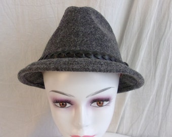 May include: A gray fedora-style hat with a braided black band. The hat has a slightly pointed crown and a brim that curves up slightly. The hat is made of a felt-like material.