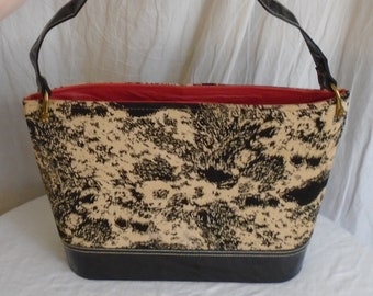 May include: A black and white patterned handbag with a black leather handle and a red lining. The bag has a rounded shape and a black leather bottom.