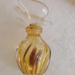 May include: A vintage perfume bottle with a clear, bird-shaped stopper. The bottle has a swirled design in shades of amber and brown. The bottle is small and decorative.