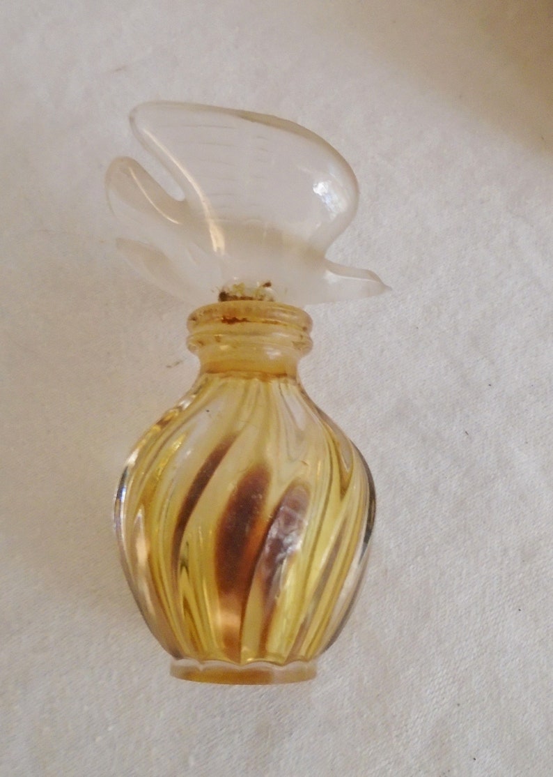 May include: A vintage perfume bottle with a clear, bird-shaped stopper. The bottle has a swirled design in shades of amber and brown. The bottle is small and decorative.