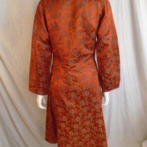May include: A long, orange, brocade coat with a mandarin collar. The coat has a floral pattern in a darker shade of orange.