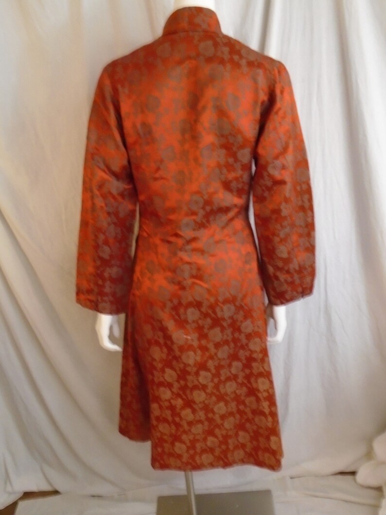 May include: A long, orange, brocade coat with a mandarin collar. The coat has a floral pattern in a darker shade of orange.