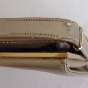 May include: A beige handbag with a gold-colored clasp and strap. The bag's strap is stitched and shows some wear. The clasp is rectangular and the bag appears to be made of a smooth material.