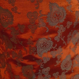 May include: Red fabric with a dark gray floral pattern. The fabric has a subtle sheen and a textured surface.
