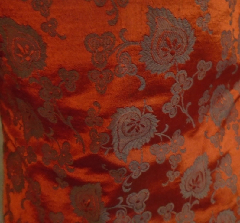 May include: Red fabric with a dark gray floral pattern. The fabric has a subtle sheen and a textured surface.