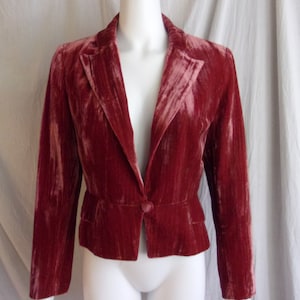 Può includere: Un blazer in velluto bordeaux con chiusura a un bottone. La giacca presenta revers a lancia, due tasche anteriori e una vestibilità su misura. Il tessuto ha un aspetto morbido e strutturato.