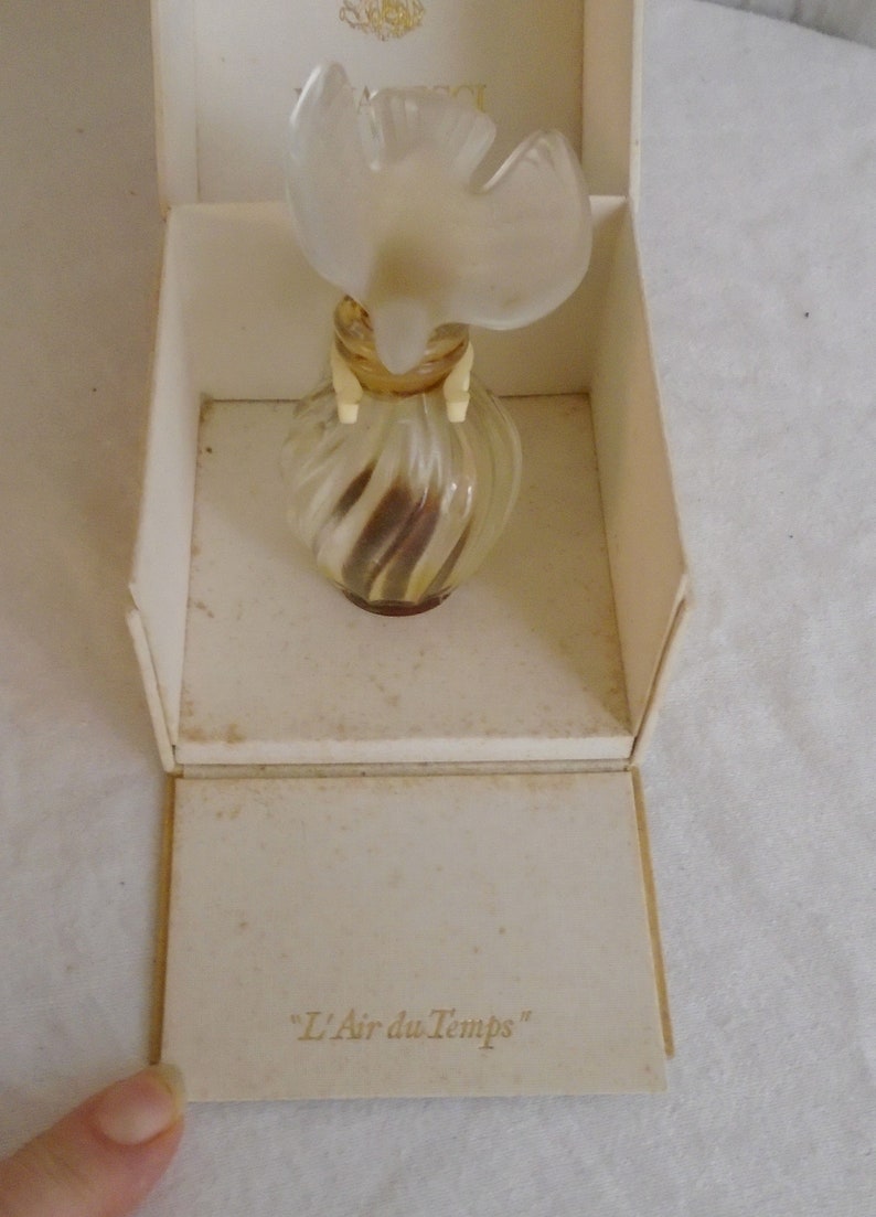 May include: A vintage perfume bottle of "L'Air du Temps" in its original box. The bottle is clear with a swirl design and a dove-shaped stopper. The box is off-white with the perfume name printed on the inside.
