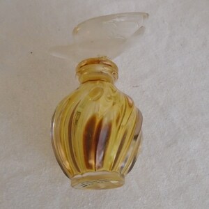 May include: A vintage perfume bottle with a clear, bird-shaped stopper. The bottle is a swirl design in shades of amber and brown. The bottle is likely made of glass.