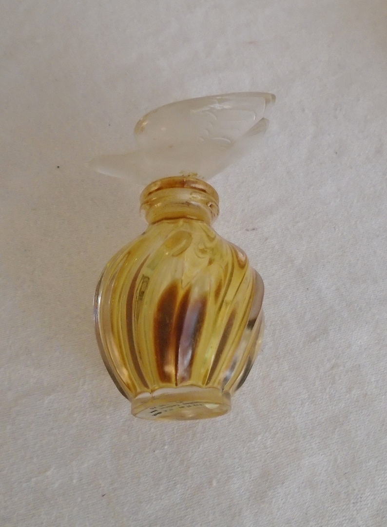 May include: A vintage perfume bottle with a clear, bird-shaped stopper. The bottle is a swirl design in shades of amber and brown. The bottle is likely made of glass.