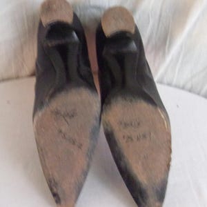Peut inclure: Une paire de chaussures en cuir noir avec des bouts pointus et de petits talons. Les semelles sont us&eacute;es et montrent des signes d'utilisation. Les talons sont de couleur marron clair.