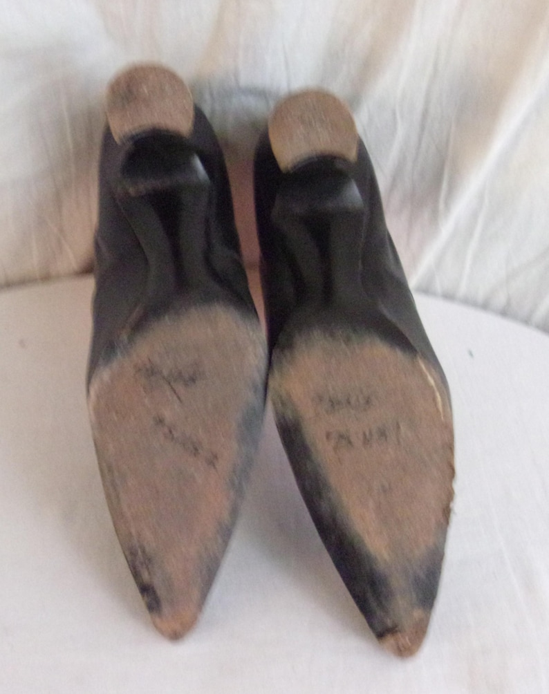 Peut inclure: Une paire de chaussures en cuir noir avec des bouts pointus et de petits talons. Les semelles sont us&eacute;es et montrent des signes d'utilisation. Les talons sont de couleur marron clair.
