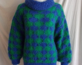May include: A blue and green patterned sweater with a turtleneck collar. The sweater features a diamond pattern in shades of blue and green. The sleeves and hem are solid blue.