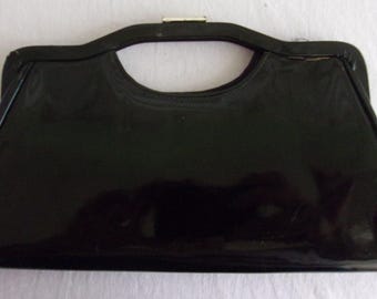 以下が含まれることがあります： 光沢のあるヴィンテージの黒いハンドバッグ。長方形のハンドバッグは、丸みを帯びたハンドルとシルバー色の留め金が特徴です。バッグのデザインはシンプルでエレガントで、さまざまな場面に適しています。