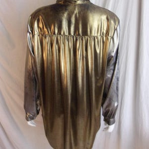 May include: A metallic gold long-sleeve shirt with a button-down collar. The shirt has a shiny, reflective surface and a gathered detail at the back yoke. The sleeves transition to a darker, greyish tone.