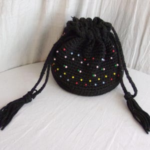 Könnte beinhalten: Schwarze gehäkelte Kordeltasche mit bunten Perlen. Die Tasche hat zwei lange Quasten.