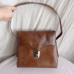 May include: A brown leather shoulder bag with a snakeskin pattern and a gold-toned clasp.