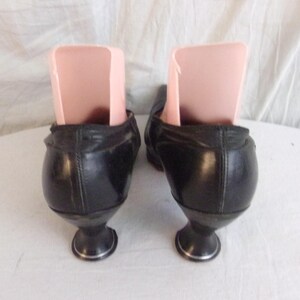 Peut inclure: Une paire de chaussures noires vintage avec des talons arrondis uniques et une bordure argent&eacute;e. Les chaussures ont un design classique, avec une coupe basse et une finition en cuir lisse. Des embauchoirs sont ins&eacute;r&eacute;s &agrave; l'int&eacute;rieur des chaussures.