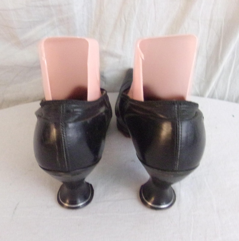 Peut inclure: Une paire de chaussures noires vintage avec des talons arrondis uniques et une bordure argent&eacute;e. Les chaussures ont un design classique, avec une coupe basse et une finition en cuir lisse. Des embauchoirs sont ins&eacute;r&eacute;s &agrave; l'int&eacute;rieur des chaussures.