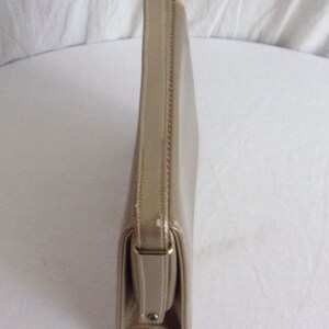 May include: A beige clutch purse with a rectangular shape and a handle. The purse has a flap closure with a gold-colored metal clasp. The material appears to be leather or a leather-like material.