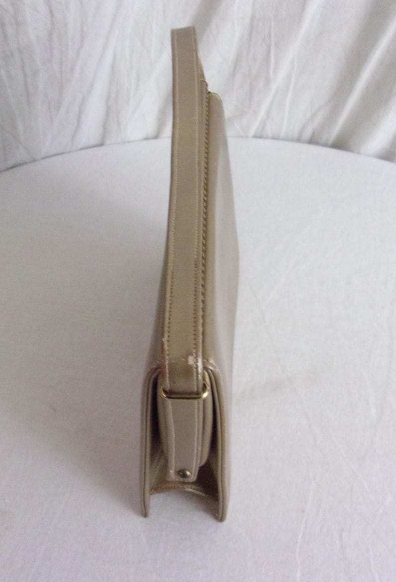 May include: A beige clutch purse with a rectangular shape and a handle. The purse has a flap closure with a gold-colored metal clasp. The material appears to be leather or a leather-like material.