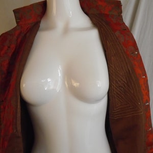 May include: A red and gold brocade jacket with a brown lining. The lining has a geometric pattern of stitching.