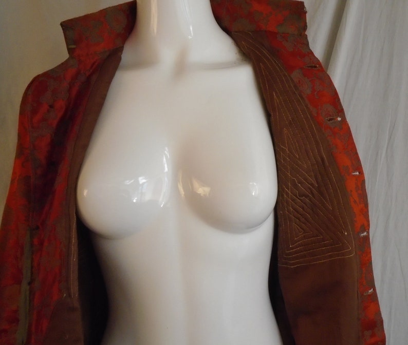 May include: A red and gold brocade jacket with a brown lining. The lining has a geometric pattern of stitching.