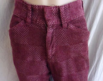 Peut inclure: Gros plan sur un pantalon bordeaux avec un motif en chevrons. Le pantalon a une fermeture boutonnée et zippée, des passants de ceinture et des poches. Le tissu semble être une matière tissée, peut-être de la laine ou un mélange de laine.
