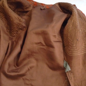 May include: The inside of a brown jacket with a quilted lining. The lining is a lighter brown color and has a geometric pattern.