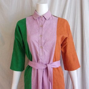 May include: A colour-blocked dress in green, lavender, and orange. The dress has a collared neckline, button-down front, and a matching belt. The sleeves are three-quarter length.