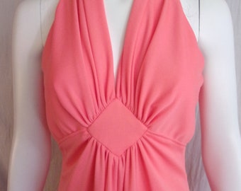 May include: A coral-colored halter dress with a deep V-neckline. The bodice features a diamond-shaped detail at the center, with gathered fabric radiating outwards. The dress is displayed on a white mannequin, showcasing its flowing design.
