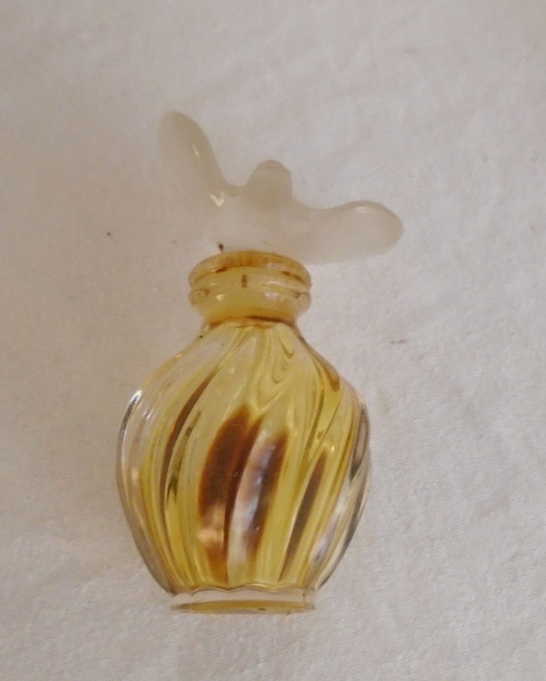 May include: A vintage perfume bottle with a swirling yellow glass body and a frosted white butterfly-shaped stopper. The bottle has a small, rounded shape and a cork closure. The glass has a subtle, swirled pattern.