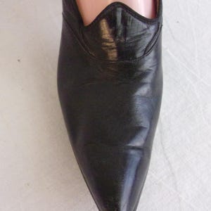 Peut inclure: Gros plan d'une chaussure en cuir noir &agrave; bout pointu. La chaussure pr&eacute;sente un bord d&eacute;coratif festonn&eacute; autour de l'ouverture. Le cuir semble l&eacute;g&egrave;rement us&eacute;, avec des plis visibles.