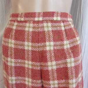 May include: Close-up of a pair of high-waisted, vintage-style trousers. The fabric features a red and cream plaid pattern with a subtle texture. The trousers have a tailored fit, with pleats at the waist.
