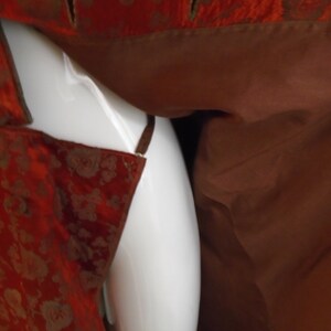 May include: A close-up of a red and gold brocade fabric with a brown lining. The fabric is draped over a white surface.