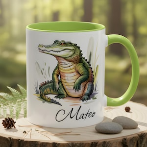 May include: White ceramic mug with a green interior and handle, featuring a watercolour illustration of a green and yellow alligator. The mug has the name "Mateo" written in cursive.