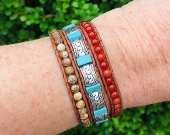 May include: A set of three bracelets stacked on a wrist. The top bracelet is made of red carnelian beads. The middle bracelet is made of brown leather with silver accents and turquoise beads. The bottom bracelet is made of brown leather with silver accents.