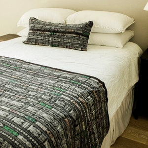 May include: A white bed with a black and white patterned throw blanket and a black and white patterned pillow. The bed has a white bed skirt.