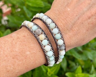 May include: A double wrap bracelet with brown leather and silver chain, featuring light green, white, and gray gemstone beads.