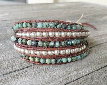 May include: A multi-wrap leather bracelet with turquoise and white pearl beads. The bracelet is brown and has a rustic look.