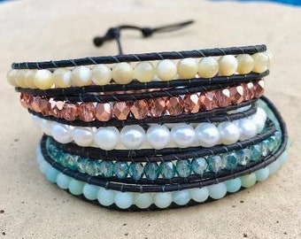 May include: A multi-strand bracelet with a black leather cord base and various beads, including white pearls, light blue, and copper-colored beads.