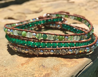 May include: A multi-strand leather wrap bracelet with green and silver beads. The bracelet is made with brown leather cord and features green glass beads, silver beads, and silver spacer beads.