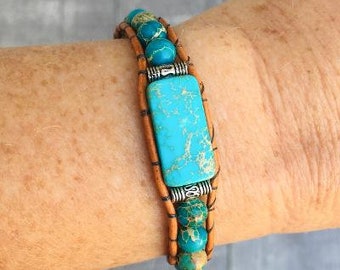 May include: A turquoise and brown leather bracelet with a rectangular turquoise stone and silver accents.