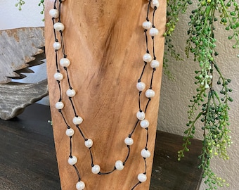 May include: A double-strand necklace with white pearls and black cord. The necklace is displayed on a wooden mannequin.