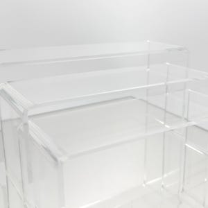 Könnte beinhalten: Set aus transparenten Acryl-Display-Erhöhungen in einer gestuften Anordnung. Das Set umfasst drei rechteckige Plattformen unterschiedlicher Größe, ideal für die Präsentation von Produkten. Das transparente Design ermöglicht optimale Sichtbarkeit.
